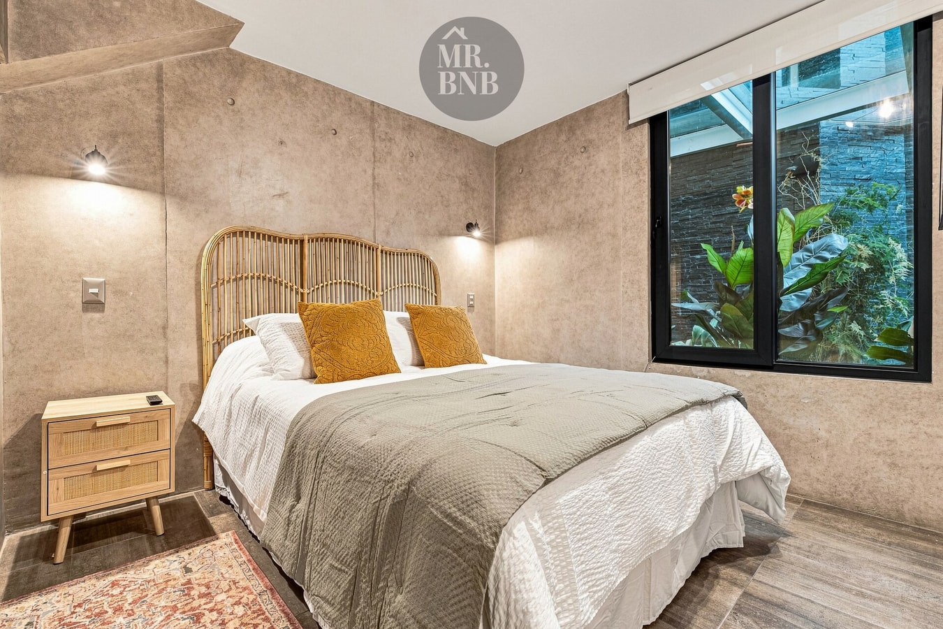 Dormitorio con cama, cojines mostaza, cabecero de mimbre y ventana