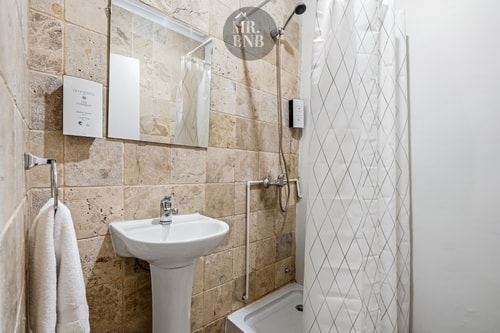 Baño con ducha, lavamanos de pedestal y azulejos en tonos beige.