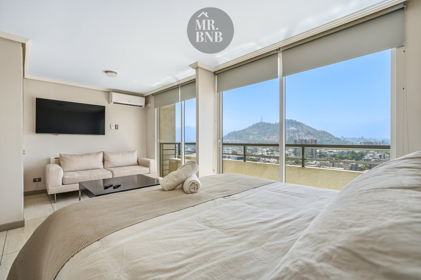 Dormitorio con cama, sofá y TV, ventanales con vista al cerro