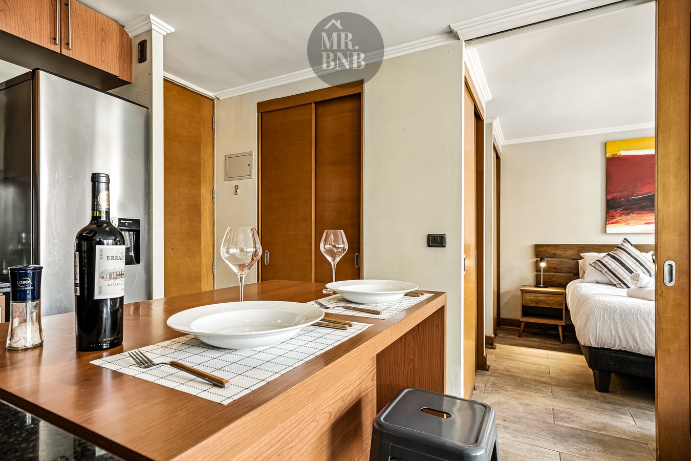Detalle de barra con vajilla y copas, dormitorio al fondo con cama y cuadro